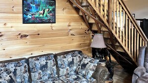 A wooden interior with a staircase, a sofa with animal prints, and a framed picture on the wall. - Rustic and all the comforts of home in the Heart of the Elk Range (Benezette)