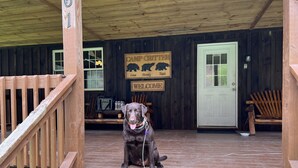 A wooden porch with a dog sitting on steps, a sign reading "Camp Cottier," and a door with a "No Smoking" sign. - Rustic and all the comforts of home in the Heart of the Elk Range (Benezette)