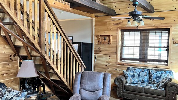 A wooden interior with a staircase, a ceiling fan, a sofa, a chair, and a patterned rug. - Rustic and all the comforts of home in the Heart of the Elk Range (Benezette)