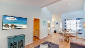 Un vaste espace de vie comprenant un coin repas, un canapé et un tableau représentant une scène de plage.