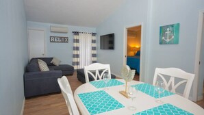 Un salon avec un canapé, une table à manger et des chaises, un téléviseur et un panneau indiquant « RELAX ».