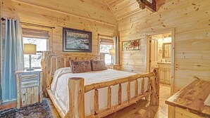 Un dormitori de cabana de fusta amb llit, una taula de nit, un armari i una finestra amb cortines.