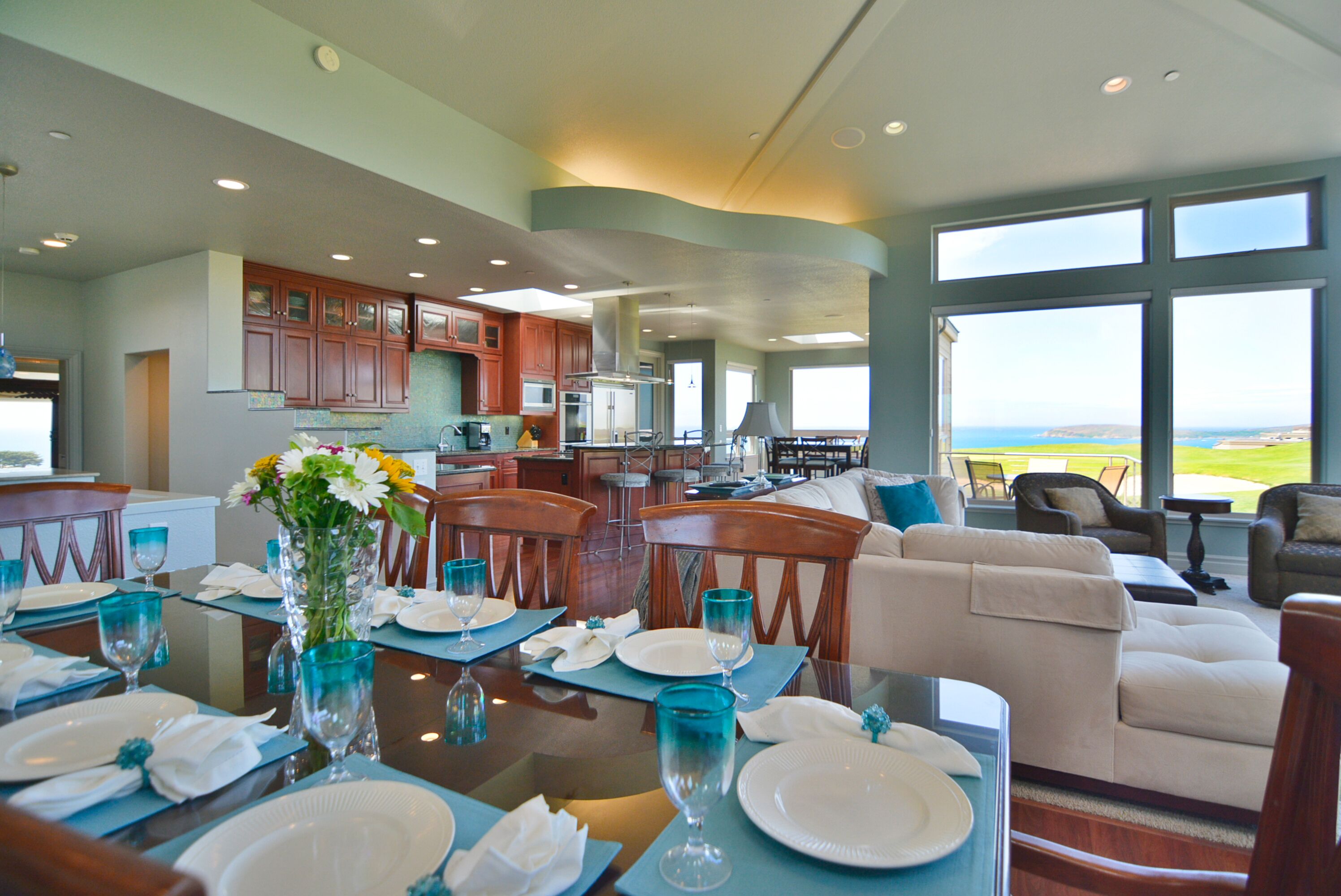 A spacious dining area with a table set for a meal, a living room with a sofa and chairs, and a kitchen in the background.