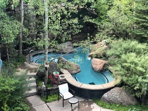 A hot tub surrounded by rocks and greenery, with a chair and table nearby.