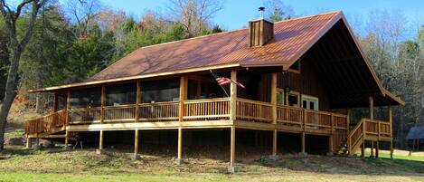 A rustic cabin with a wooden deck, large windows, and a chimney.