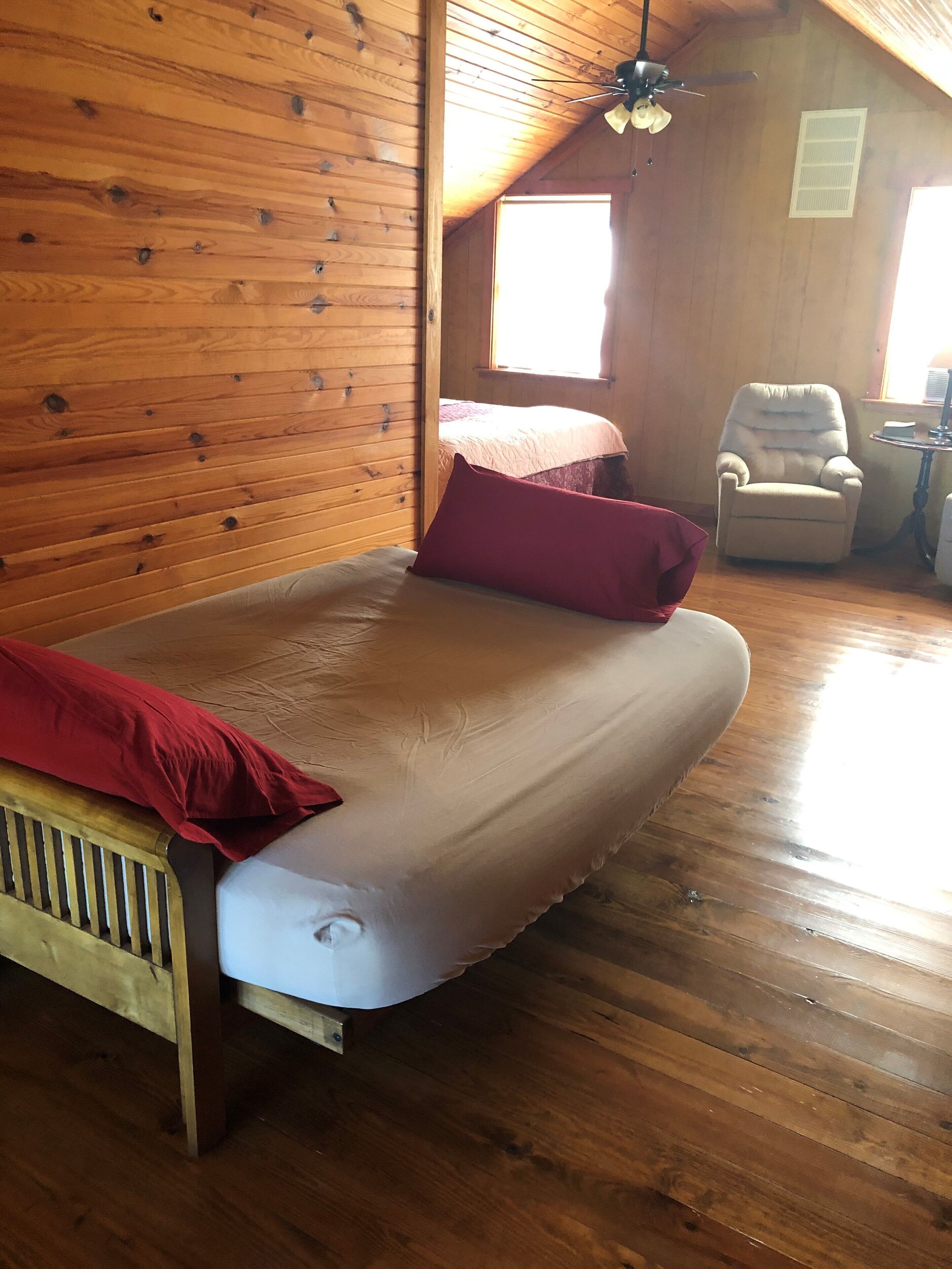 Una habitación de madera con una cama, una silla y un ventanal.