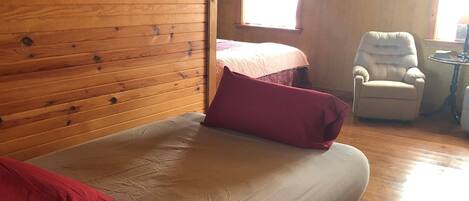 Una habitación de madera con una cama, una silla y un ventanal.
