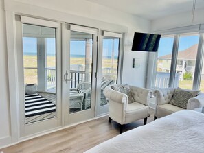 A room with a large sliding glass door leading to a balcony with a view of the beach. There is a white sofa and a bed with a white duvet. - Oceanfront /Spectacular Views/"OCEAN BEACH " (Bald Head Island)