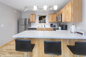 Una cocina moderna con armarios de madera, un refrigerador de acero inoxidable, un microondas y una isla grande con taburetes de bar.