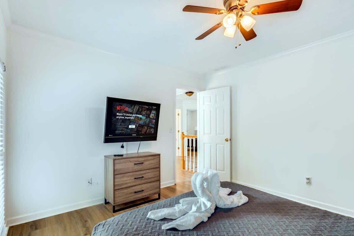 A bedroom with a television, a ceiling fan, a wooden dresser, and a door leading to another room.