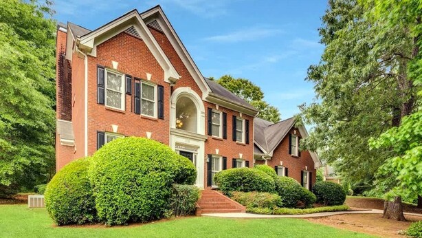 A two-story brick house with a front entrance, a covered porch, and a well-maintained lawn. - Pool oasis with workspace, sleeps 10 (Conyers)
