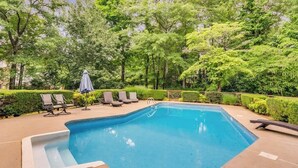 A swimming pool with lounge chairs and umbrellas, surrounded by trees and hedges. - Pool oasis with workspace, sleeps 10 (Conyers)