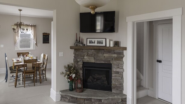 Una sala de estar con chimenea de piedra, televisor montado y comedor con candelabro.