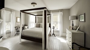Una cama con dosel, una mesita de noche con lámpara, un aparador y un cuadro en la pared.