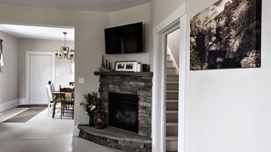Una sala de estar con chimenea de piedra, televisor montado y una escalera que sube a otro nivel.