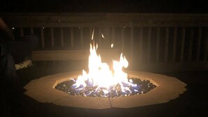 Fuego en un hogar circular al aire libre, rodeado por una terraza de madera.
