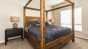 Una cama con dosel tapizada con un edredón azul oscuro y almohadas a juego, un cabecero de madera y una mesita de noche con una lámpara.