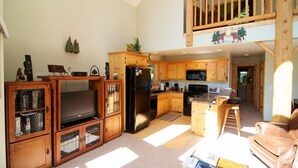 Un vaste espace de vie doté d’un grand téléviseur, de meubles en bois, d’une cuisine avec des plans de travail en bois et d’une chambre en mezzanine avec balcon.