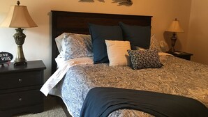 Een slaapkamer met een bed, twee nachtkastjes, een decoratie aan de muur en een bedtafeltje.