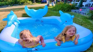 Zwei Kinder planschen in einem blauen Schwimmbecken mit Dophindekor.