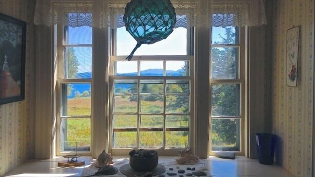 Ein Zimmer mit großen Fenstern, einer hängenden Leuchte und Blick auf eine Landschaft.