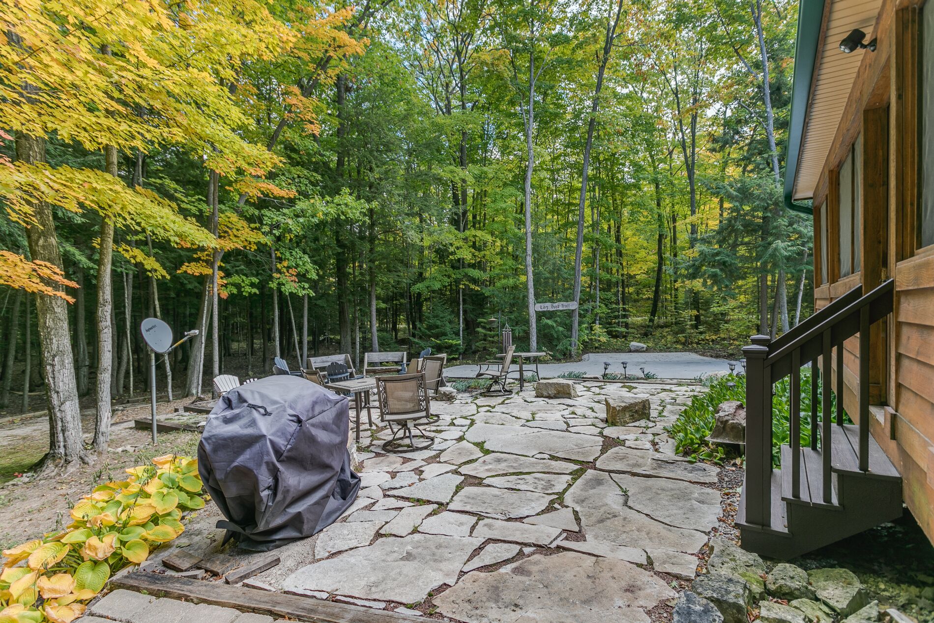 A stone patio with outdoor furniture, a covered grill, and a sign indicating a trail.