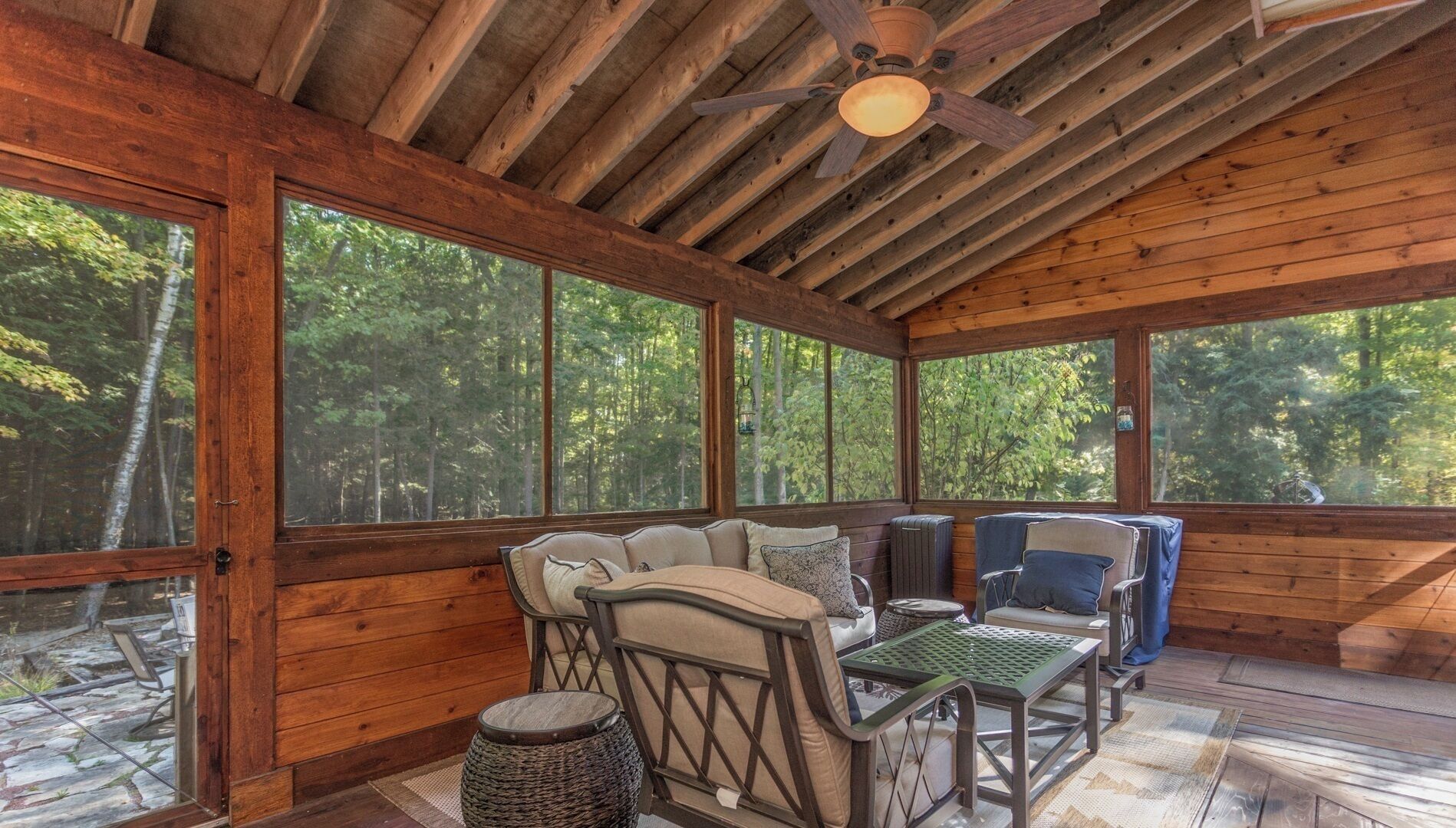 A wooden cabin with a covered porch, large windows, and a ceiling fan.
