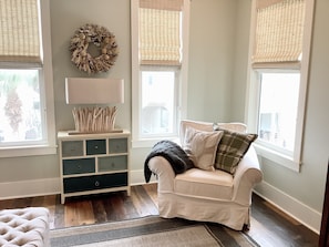 Um quarto aconchegante com uma poltrona branca, uma mesa de cabeceira de madeira, uma guirlanda decorativa e uma janela com persianas.