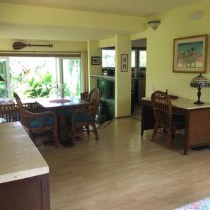 Un comedor amplio con muebles de madera, una cocina al fondo y vistas a la vegetación a través del ventanal.