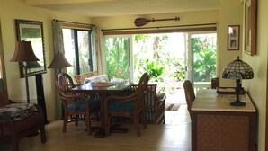 A dining area with a wooden table and chairs, a lamp, and a view of greenery through large windows. - Spacious, Comfortable with Full Kitchen & W/D (Princeville)
