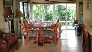 A dining area with a wooden table and chairs, a large window with a view of greenery, and a ceiling-mounted paddle. - Spacious, Comfortable with Full Kitchen & W/D (Princeville)