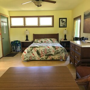 Un dormitorio con una cama, dos mesitas de noche, un escritorio, una silla, un ventilador de techo y una ventana.