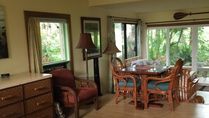 A room with a bed, a wooden dresser, a dining table with chairs, a lamp, and a window with a view of greenery. - Spacious, Comfortable with Full Kitchen & W/D (Princeville)