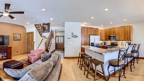 A spacious living room with a fireplace, a dining area with a kitchen in the background, and large windows offering views of the outdoors. - Breckenridge 3 Bedrm Townhouse, Private Hot Tub, near Golf, Hiking & Bike trails (Breckenridge)