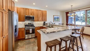 A modern kitchen with wooden cabinets, stainless steel appliances, a granite countertop, and a large island with bar stools. - Breckenridge 3 Bedrm Townhouse, Private Hot Tub, near Golf, Hiking & Bike trails (Breckenridge)