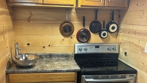 Uma cozinha compacta com armários de madeira, bancada de granito, fogão de aço inoxidável e um suporte para panelas suspenso.