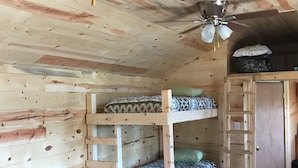 Quarto com beliche, ventoinha no teto, paredes de madeira e uma pequena escrivaninha.