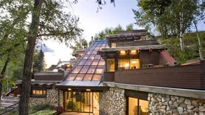 Une maison moderne avec une façade en pierre, une grande baie vitrée et une terrasse en bois.