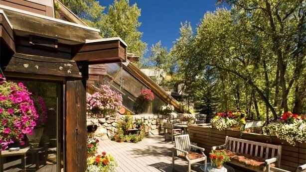 Une terrasse en bois avec des sièges d’extérieur, entourée de plantes et de fleurs en pot.