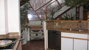 Une cuisine avec un sol carrelé en pierre, un lave-vaisselle encastré et un escalier en bois menant à un balcon.