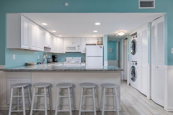 A kitchen with white cabinets, a granite countertop, and a central island with bar stools.