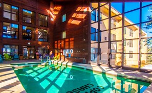 Una piscina interior moderna con paredes de vidrio transparente, rodeada de paneles de madera y ventanas grandes.