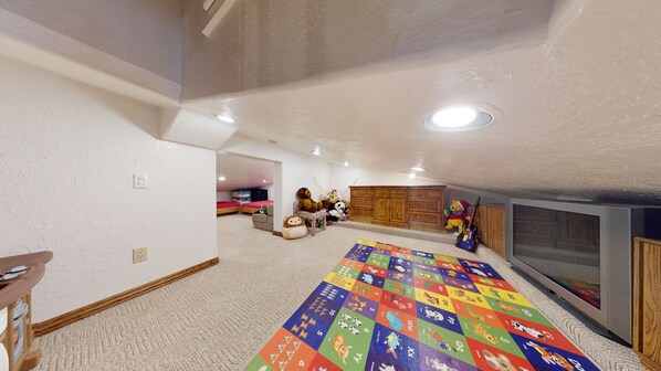 Amplia habitación en el ático con un tapete de juegos grande, muebles de madera y un televisor.