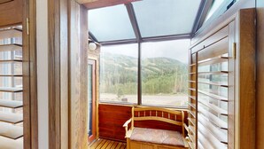 A room with a large window, a wooden bench, and a view of a forested area. - Brian Head Penthouse South, Pool-Hotub, Ski-i/o, 3 Masters, Play lofts, Sleep 14 (Brian Head)