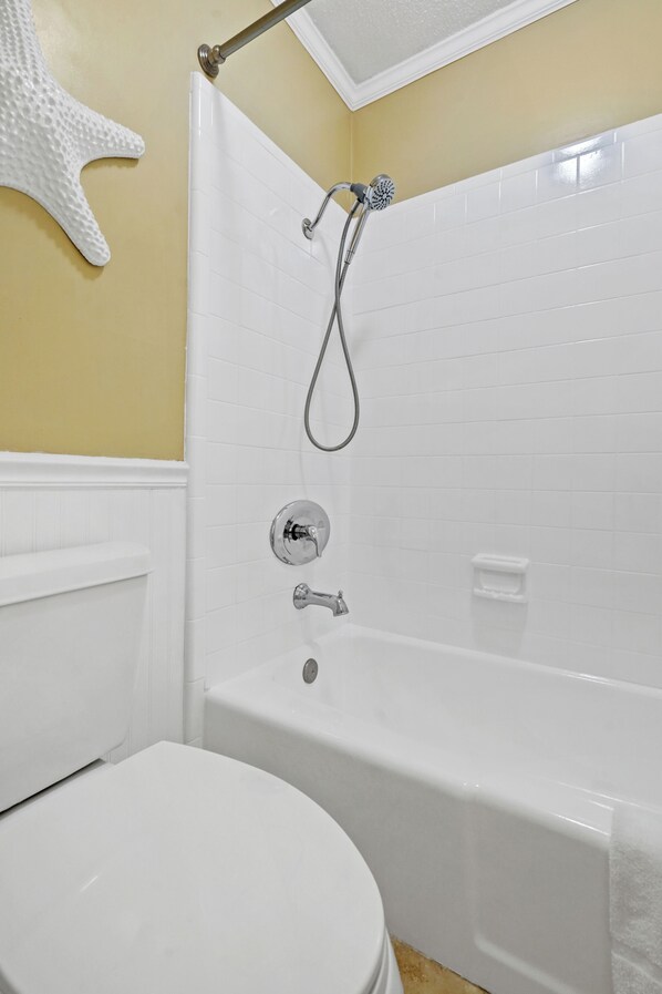 A bathroom with a white bathtub, a toilet, and a showerhead.
