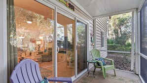 Une véranda couverte avec des portes-fenêtres coulissantes, une chaise violette, une chaise verte et une petite table.