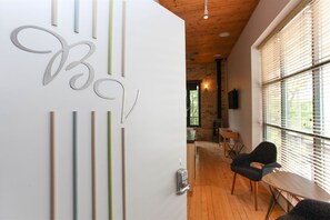 A modern interior with a white wall featuring abstract metal art, a wooden ceiling, and a view through large windows.