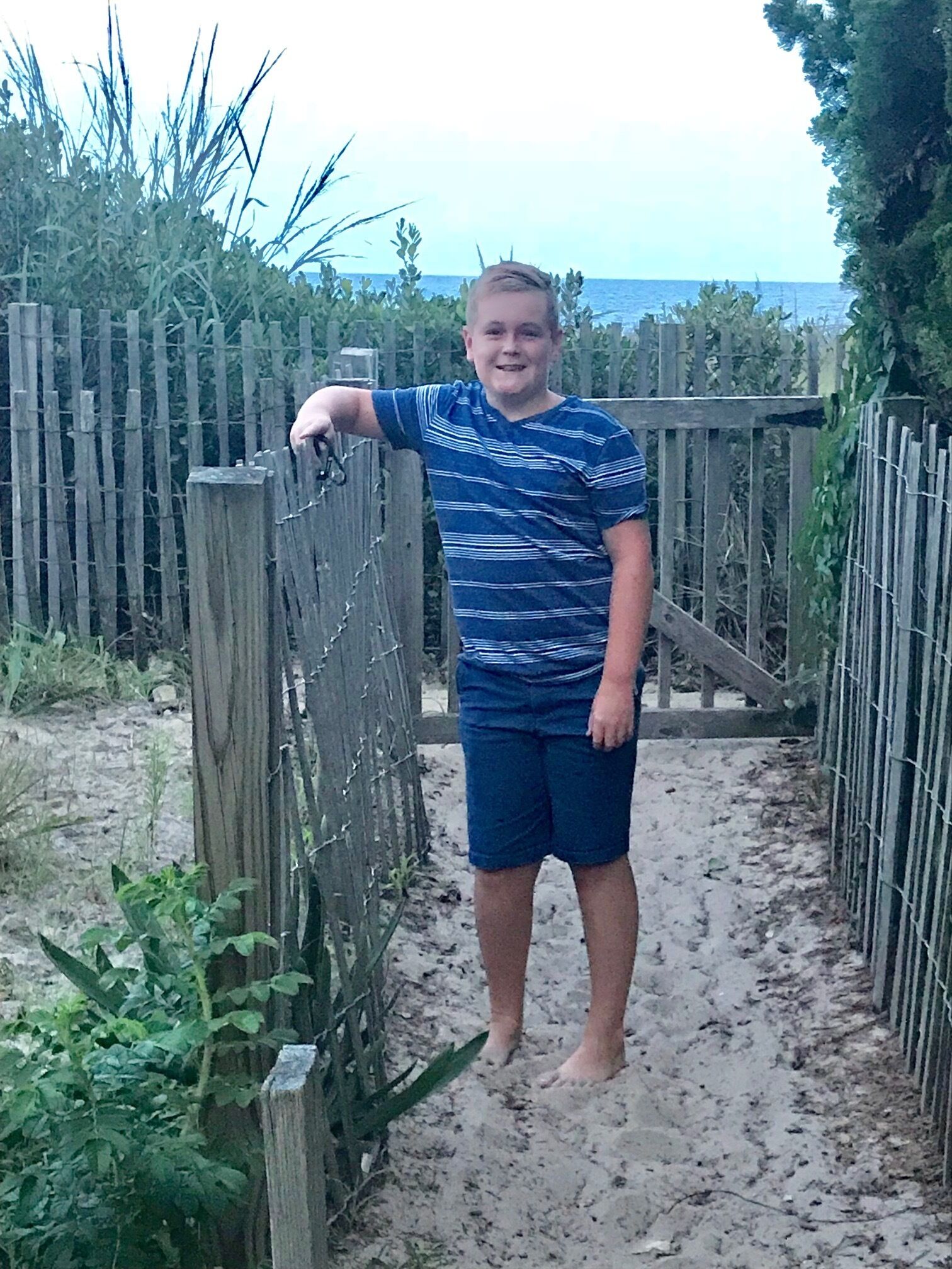 Une personne se tient sur un sentier sablonneux, à côté d’une clôture en bois.