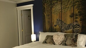 Een slaapkamer met een groot bed, een muurschildering van een zebra aan de wand en een deur met een ringlamp.
