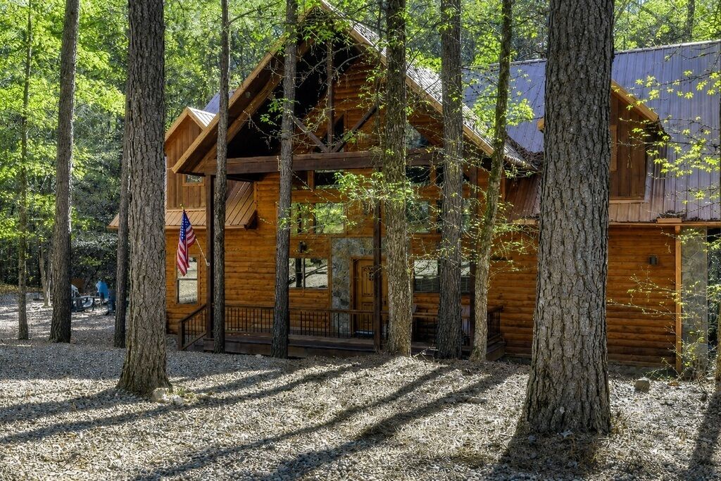 A wooden cabin surrounded by trees, with a porch and a flag.